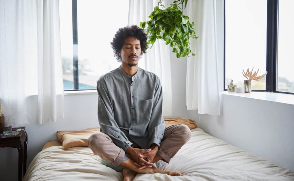 Young man meditating alone in his bedroom at home