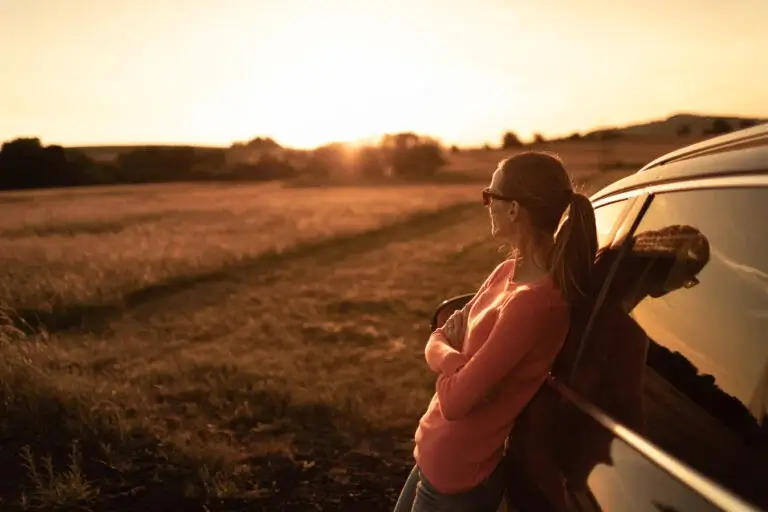 Thoughtful young woman relaxing by her car watching the beautiful sunrise.